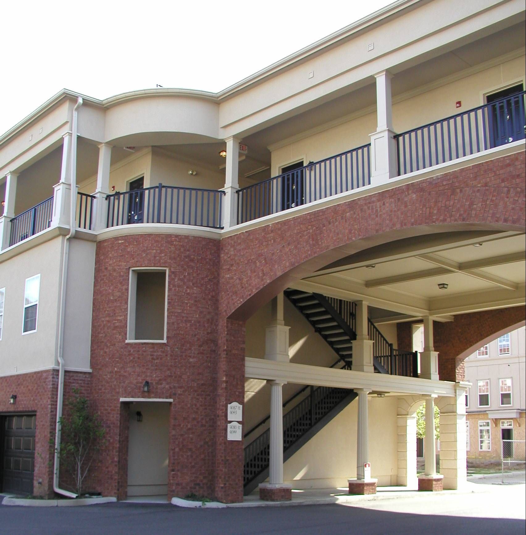 Exterior of a brick building with an elevated walkway, stairs, and covered archway entrance