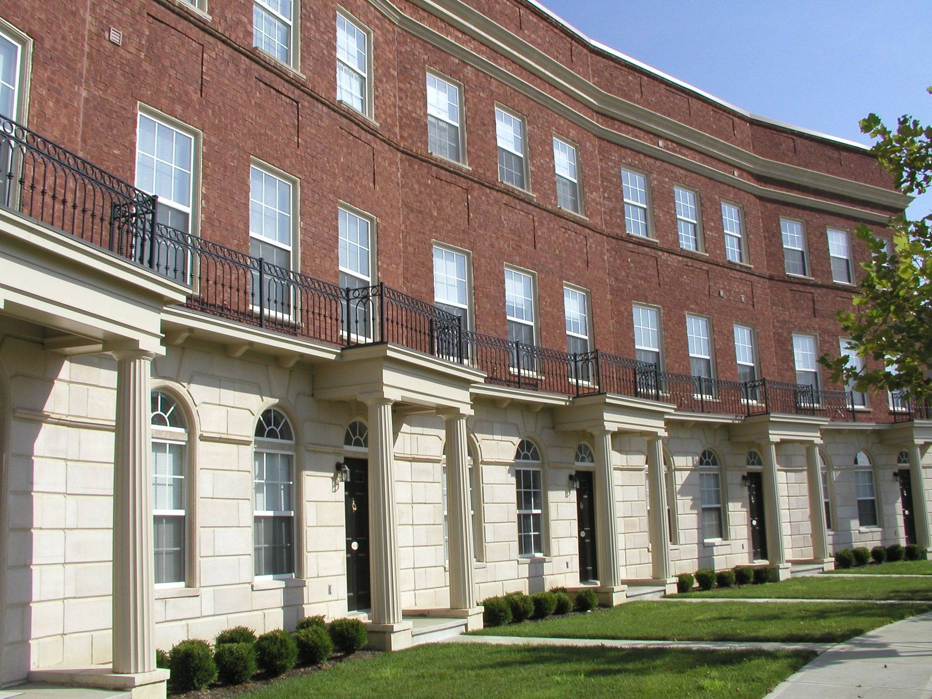 Curved red-brick building with white columns and black railings beside a green lawn