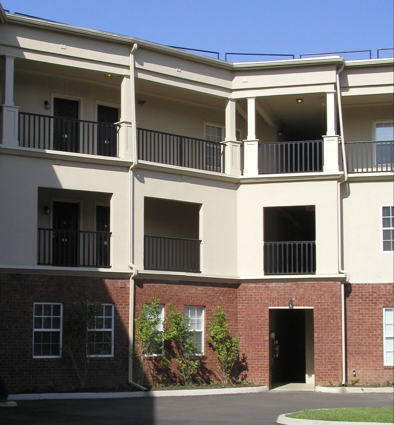 Three-story apartment building with balconies, white columns, and brick lower facade