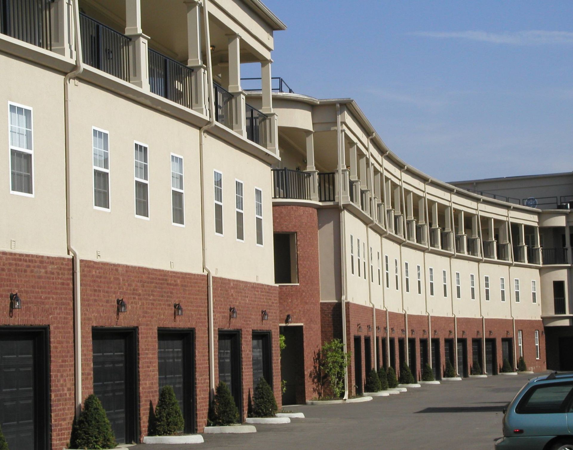 Curved beige-and-brick building with rows of windows and garages along a paved lot