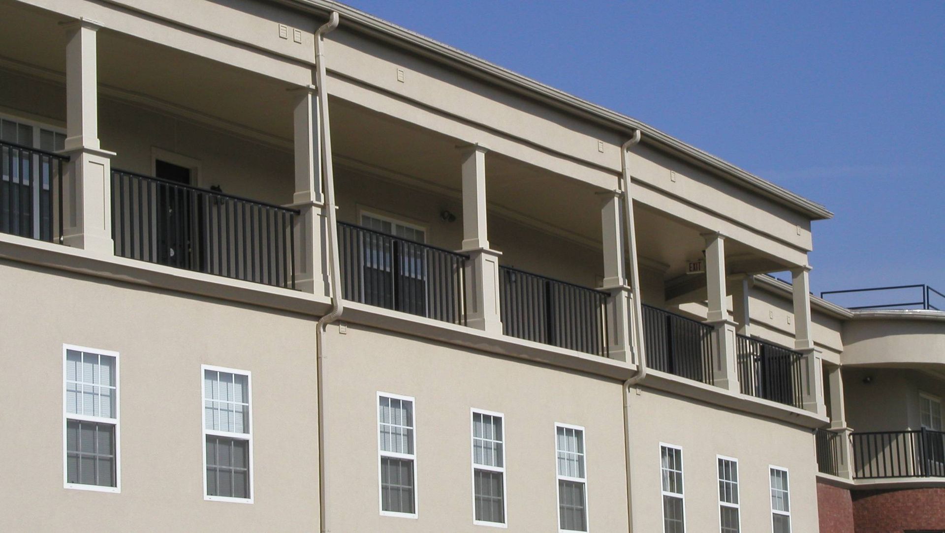 Beige apartment building with balconies and white railings under a clear blue sky