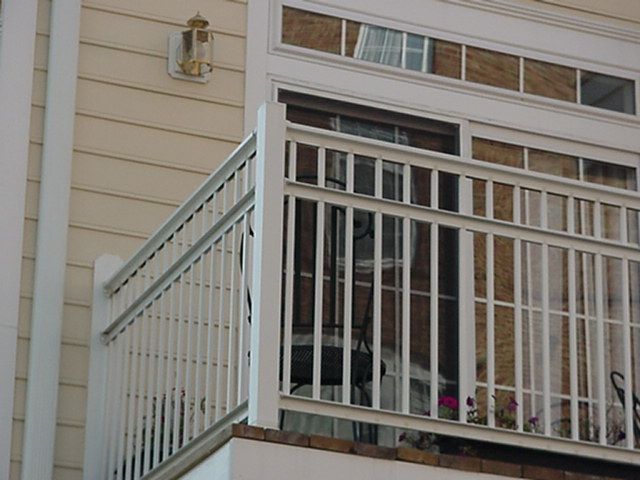 White railing and porch beside a cream-sided house with windows and a wall light.