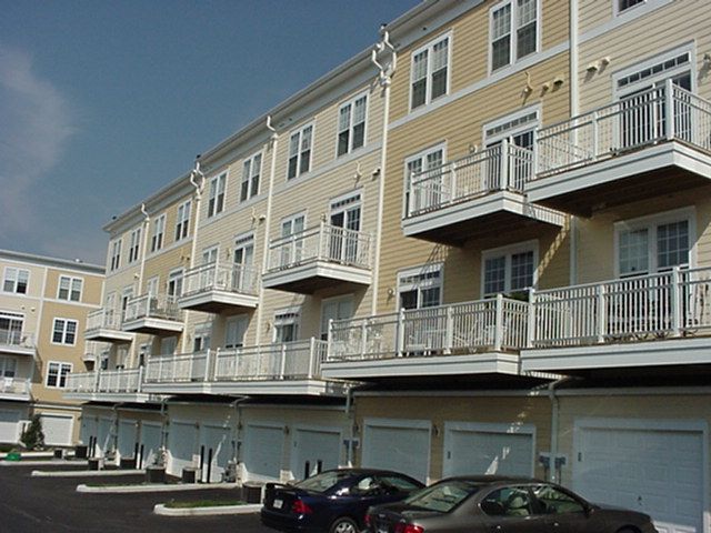 Row of beige townhouse apartments with balconies and garages, parked cars in front
