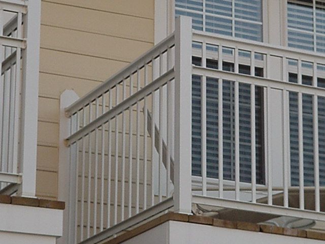 Outdoor apartment balcony with beige siding and white railings beside a window