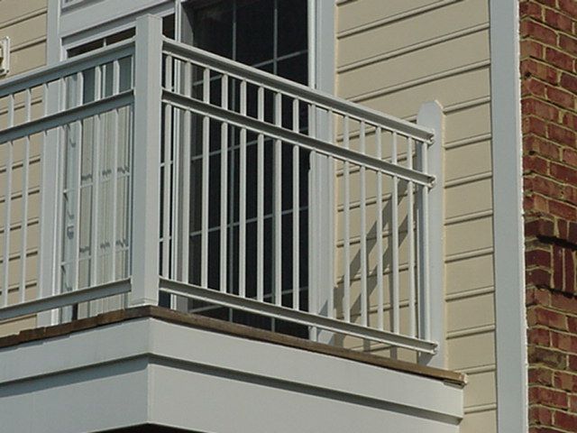 White balcony railing on a beige house with a brick wall beside it