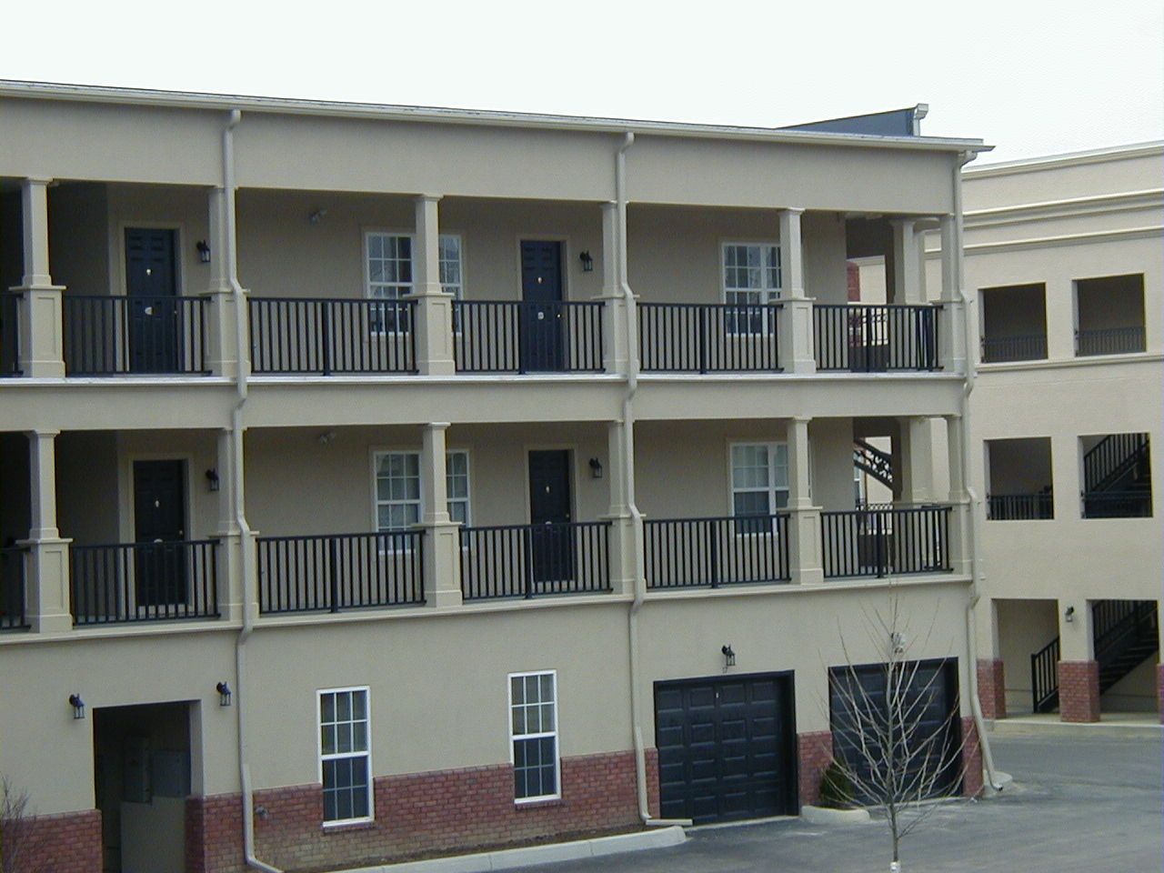 Three-story beige apartment building with balconies and dark doors, seen from a courtyard.