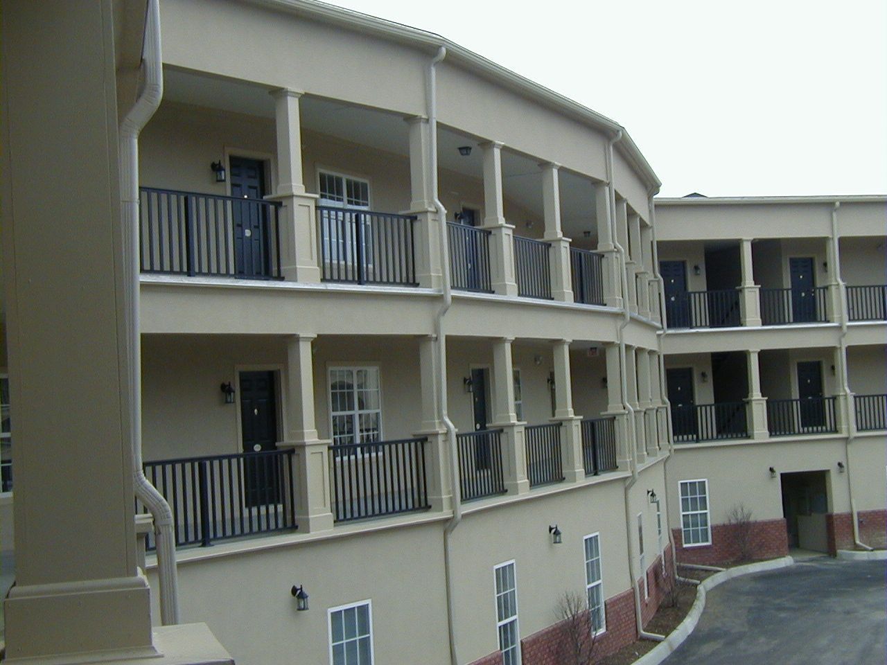 Curved beige apartment building with balconies and a paved walkway outside