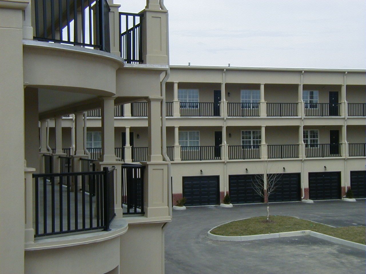 Courtyard of a beige apartment complex with balconies and garage doors along a curved driveway