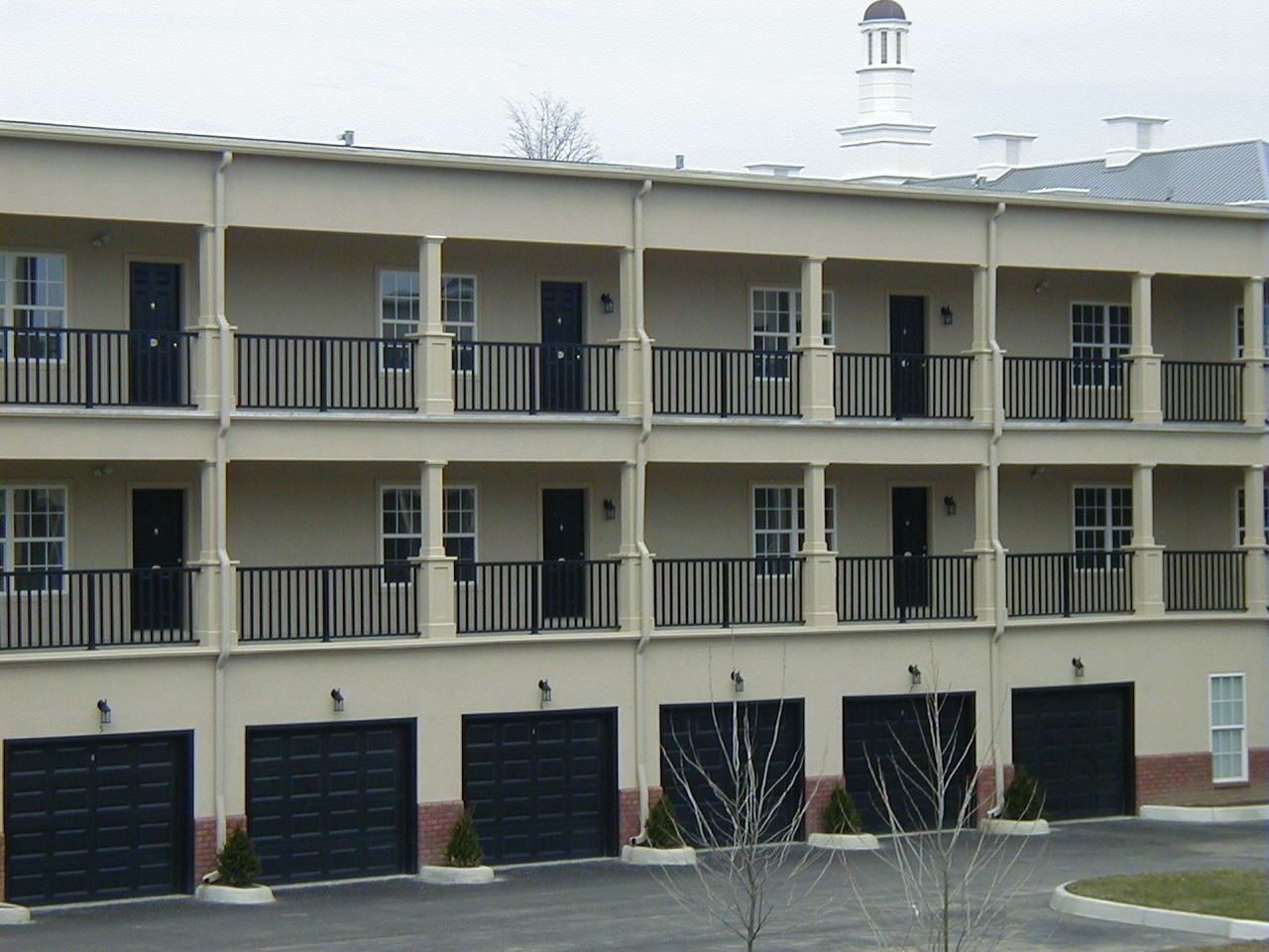 Two-story beige apartment building with black balconies and garage doors on the ground floor