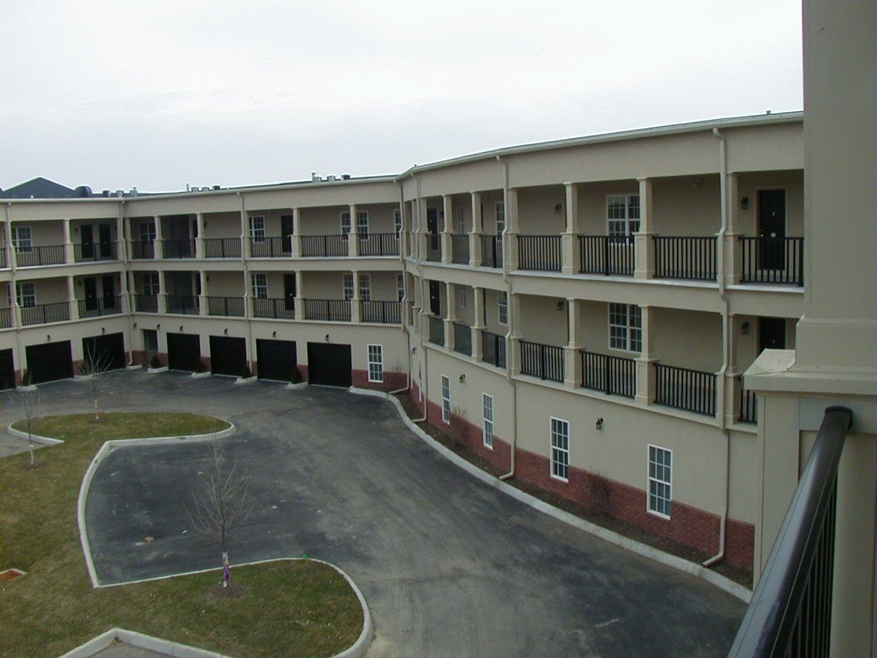 Three-story apartment complex with beige balconies and a curved driveway in front