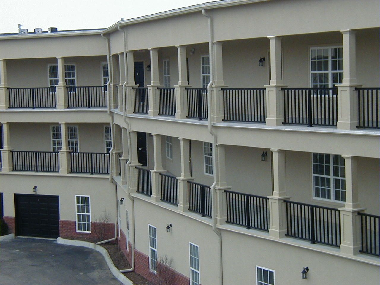 Apartment building with beige balconies and black railings, viewed from an angled exterior courtyard.