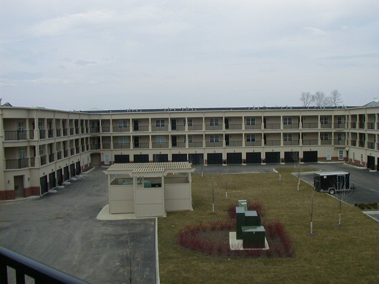 Courtyard of a beige apartment complex with grass, walkways, and utility boxes under an overcast sky