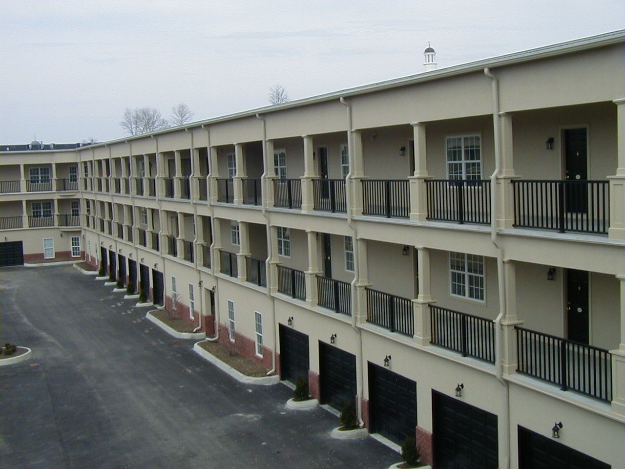 Motel-style apartment building with balconies and garage doors along a paved driveway