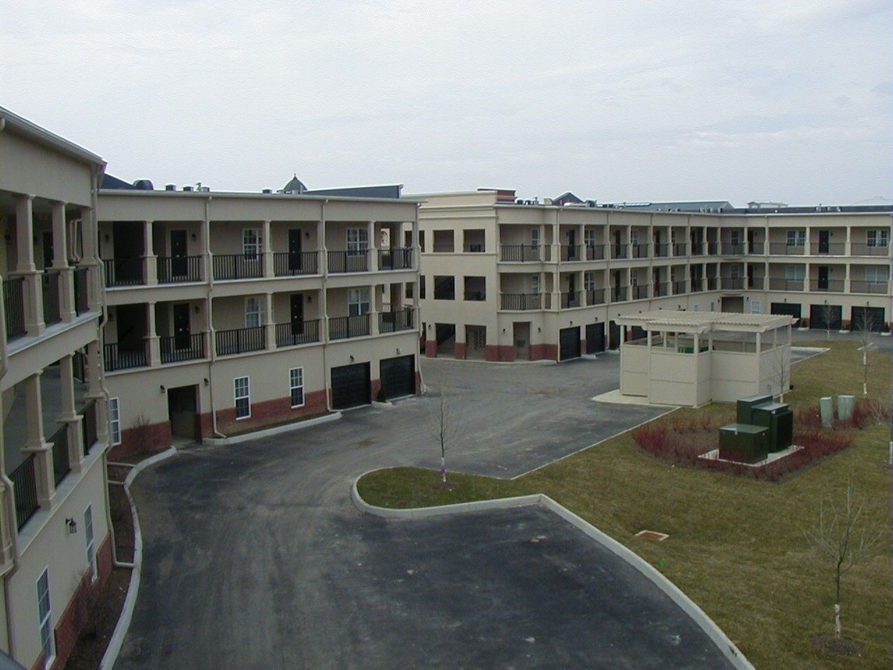 Apartment complex courtyard with curved driveway, grass, and overcast sky