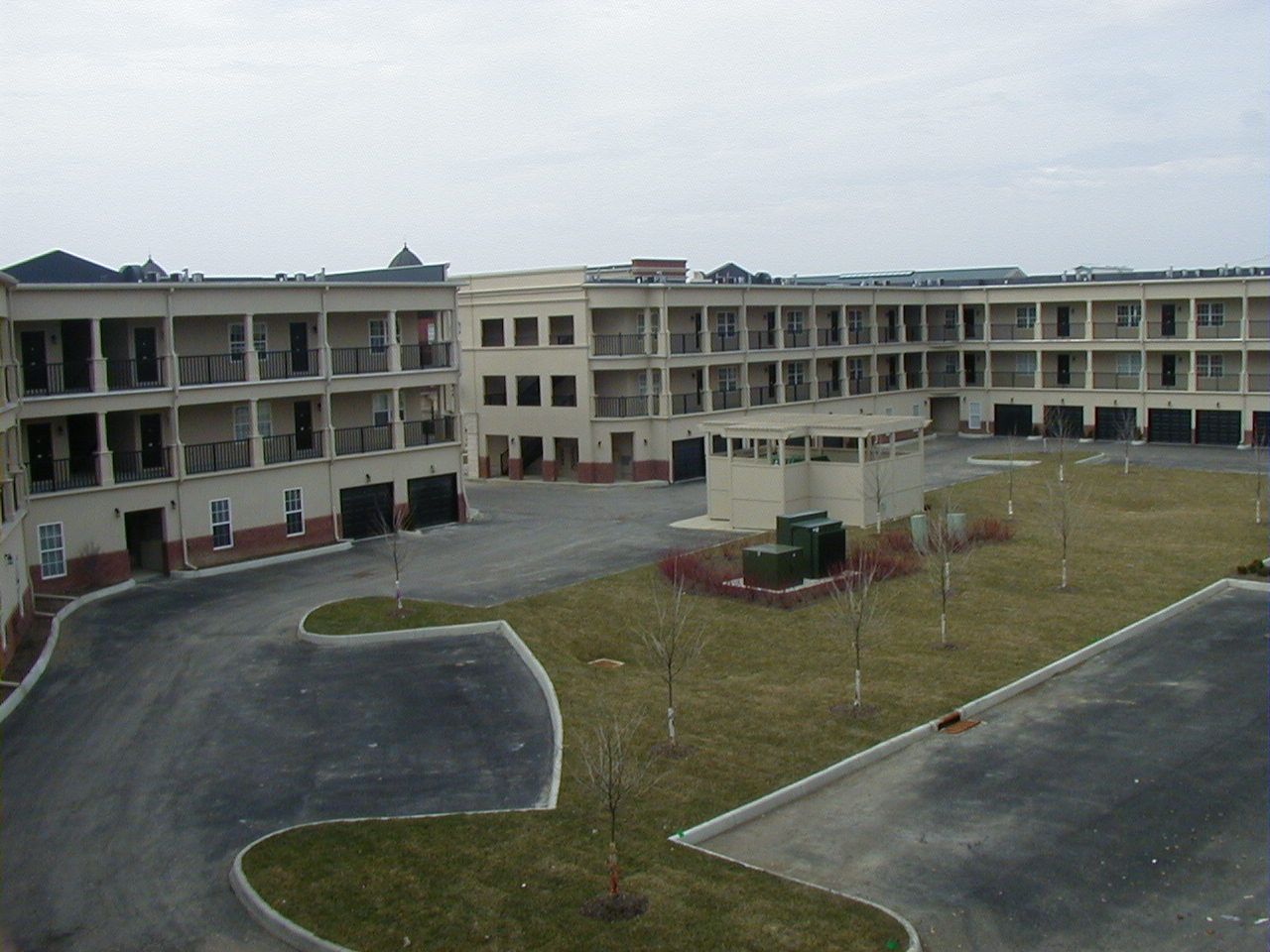 A motel courtyard with curved driveways, a grassy center, and beige three-story buildings under an overcast sky