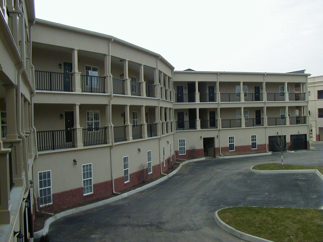 Curved apartment building with balconies and a paved driveway in front