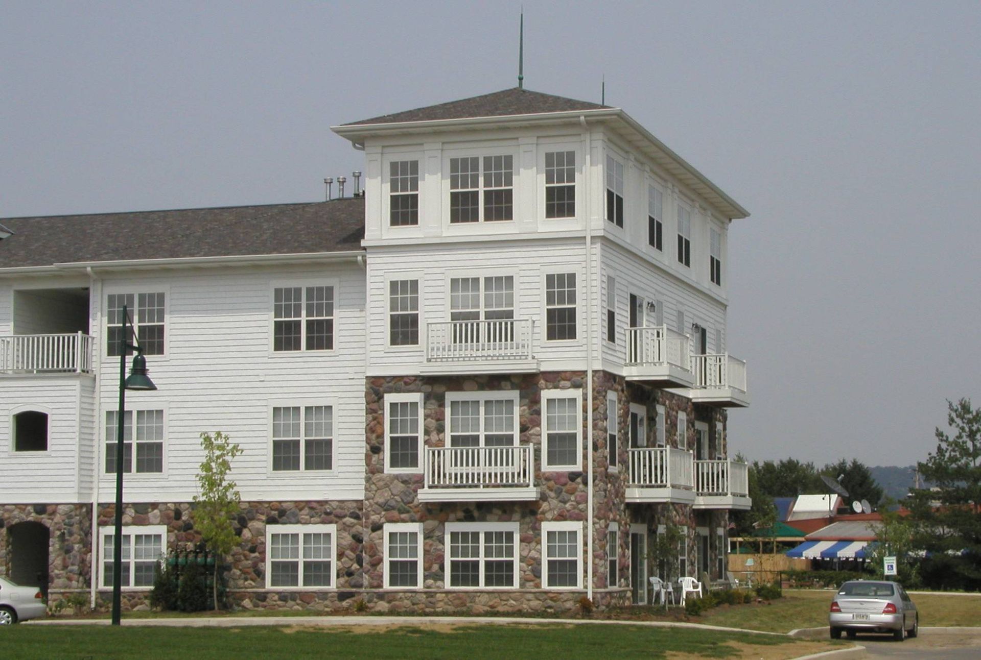 Multi-story white building with stone base beside a road, with a parked car and cloudy sky.