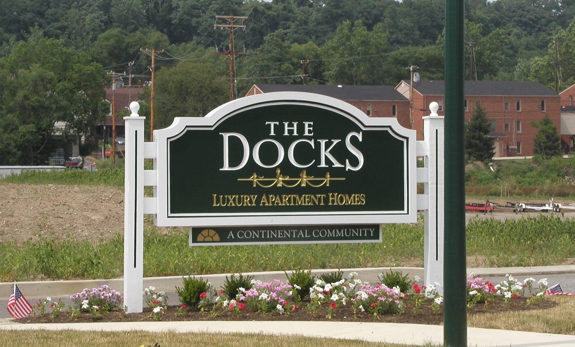 The Docks entrance sign in a landscaped area, with flowers and buildings in the background