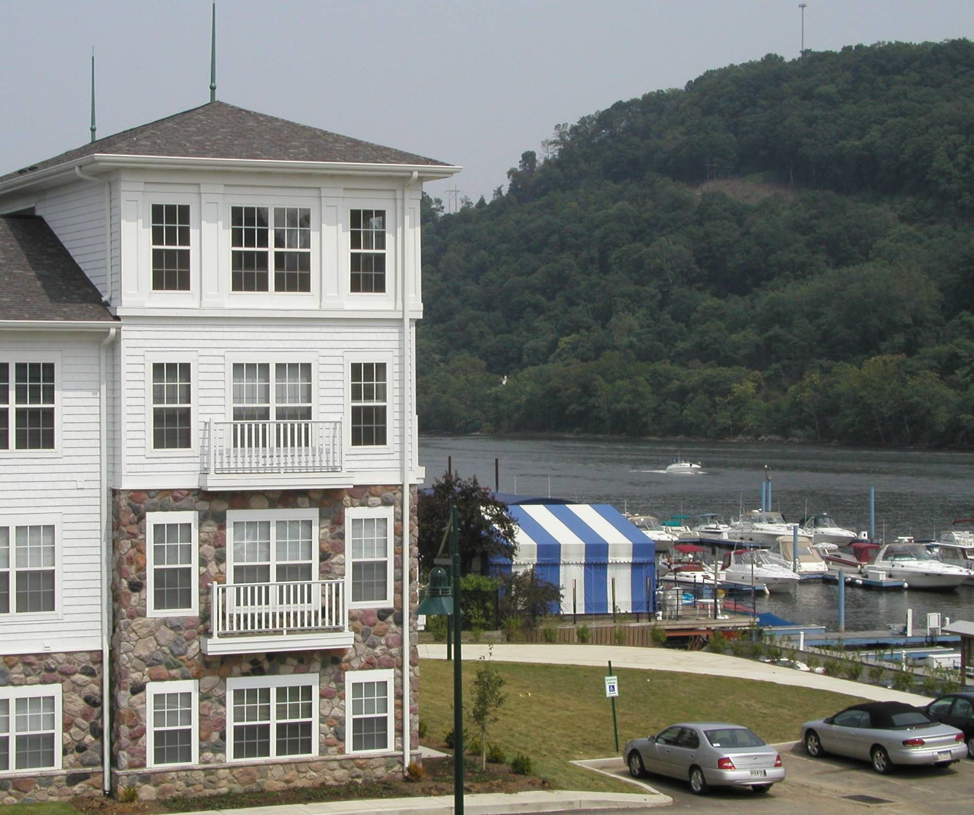 Coastal inn beside a marina, with parked cars and a wooded hillside in the background.