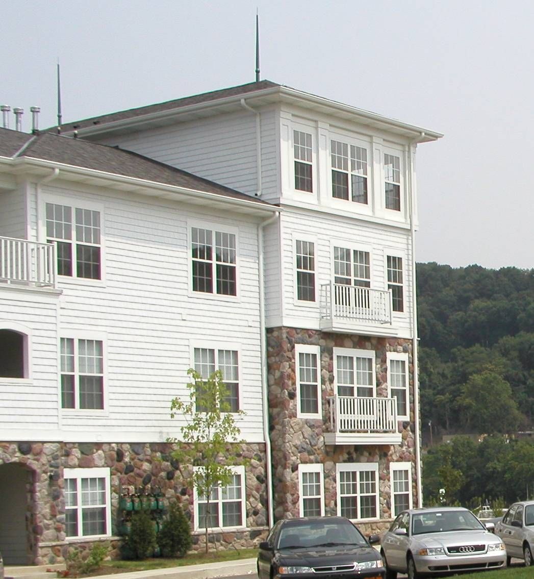 White multi-story apartment building with parked cars in front and trees in the background