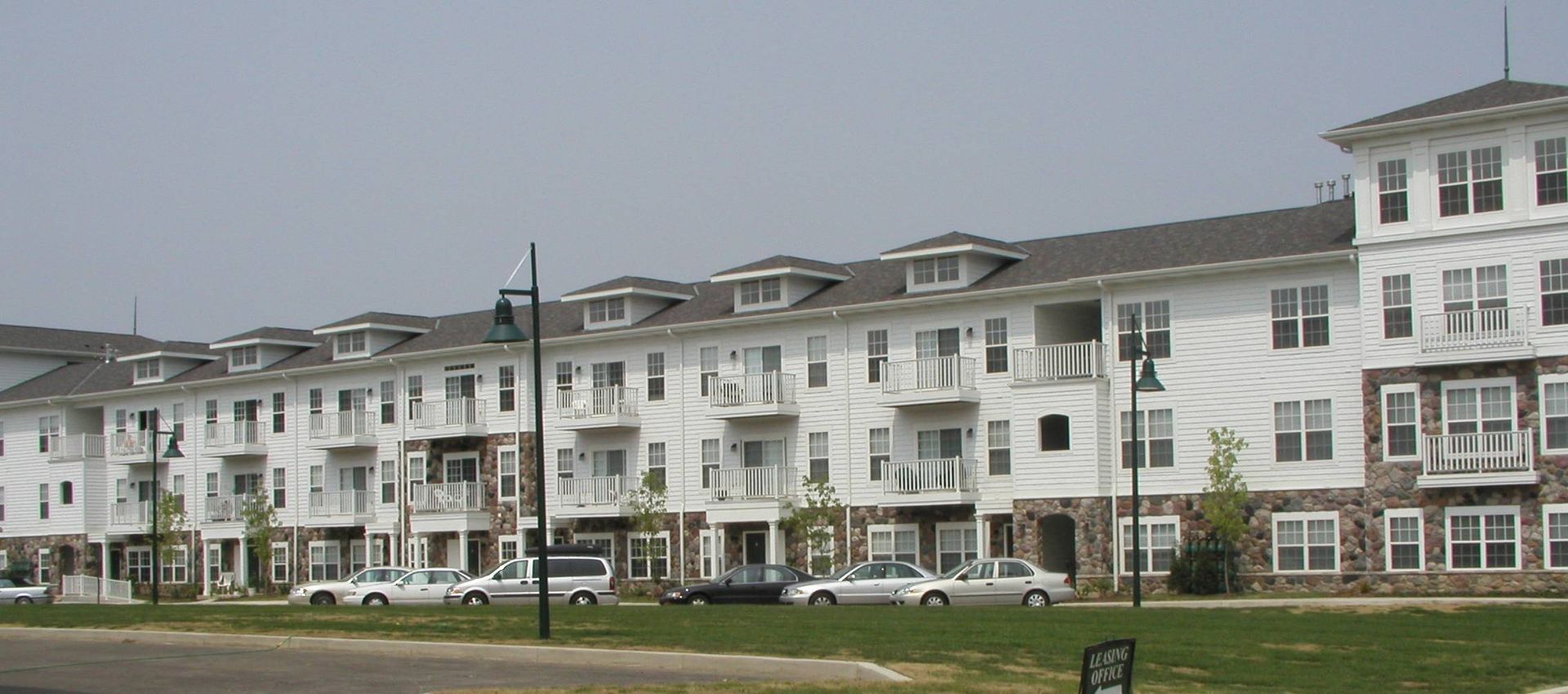 Row of white multi-story apartment buildings with parked cars along a grassy street