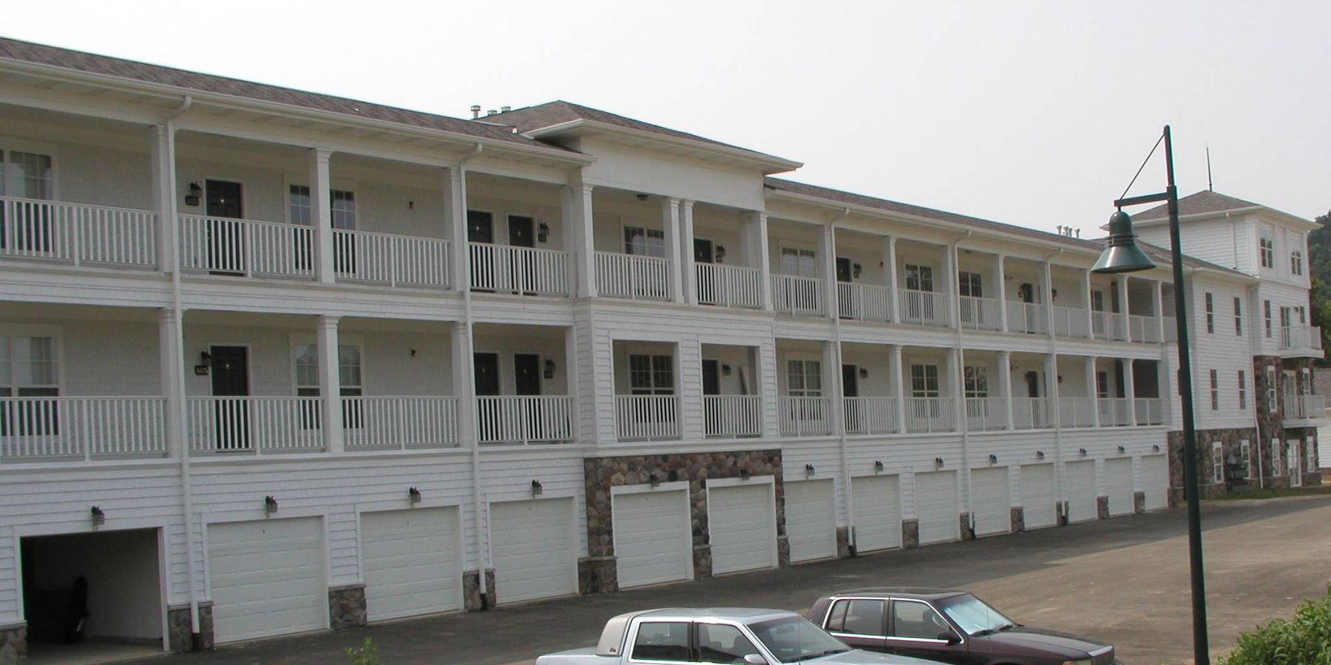 Long white apartment building with balconies and garage doors along an empty street
