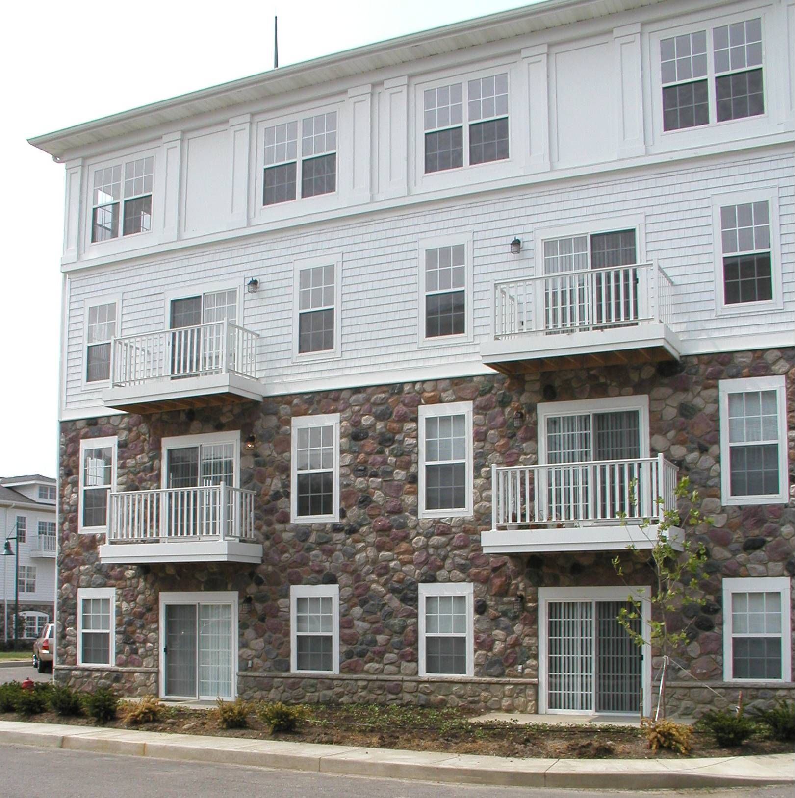 Three-story apartment building with white siding and brick lower level, featuring balconies and multiple windows