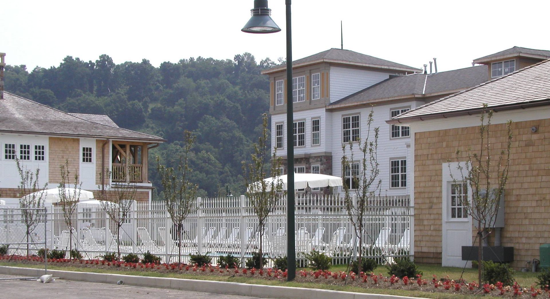 White houses with a fenced courtyard and flowers, set against a wooded hillside under a streetlamp.