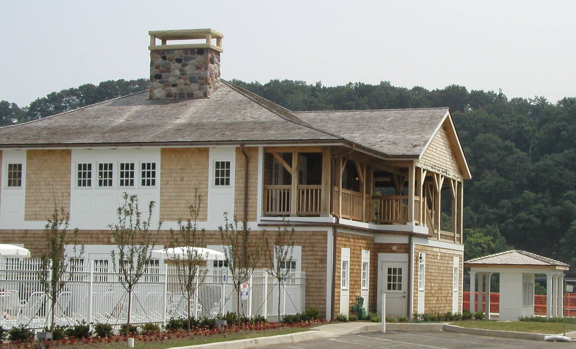 Two-story white house with wooden porch and stone chimney on a grassy hillside