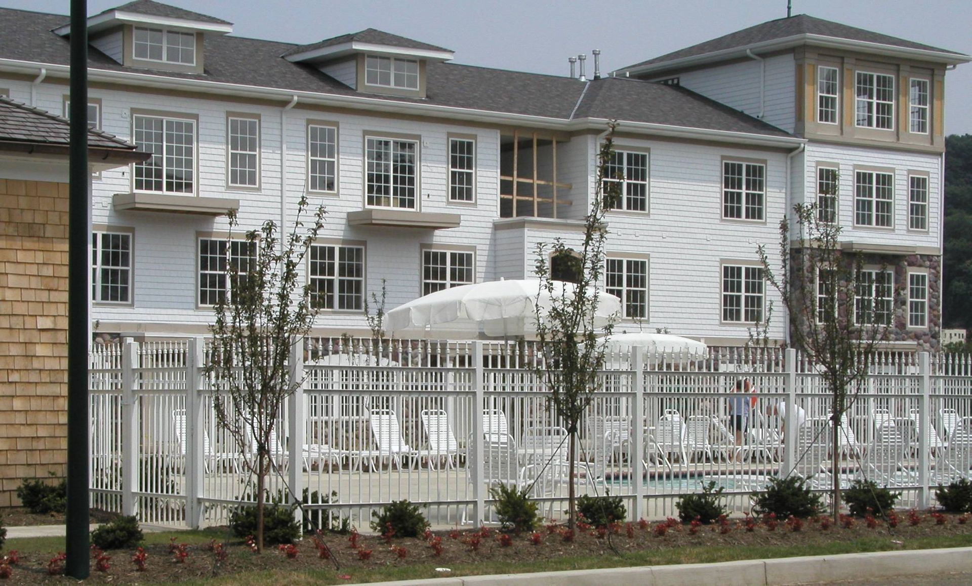 White multi-story building behind a metal fence and trees, with parked cars in front