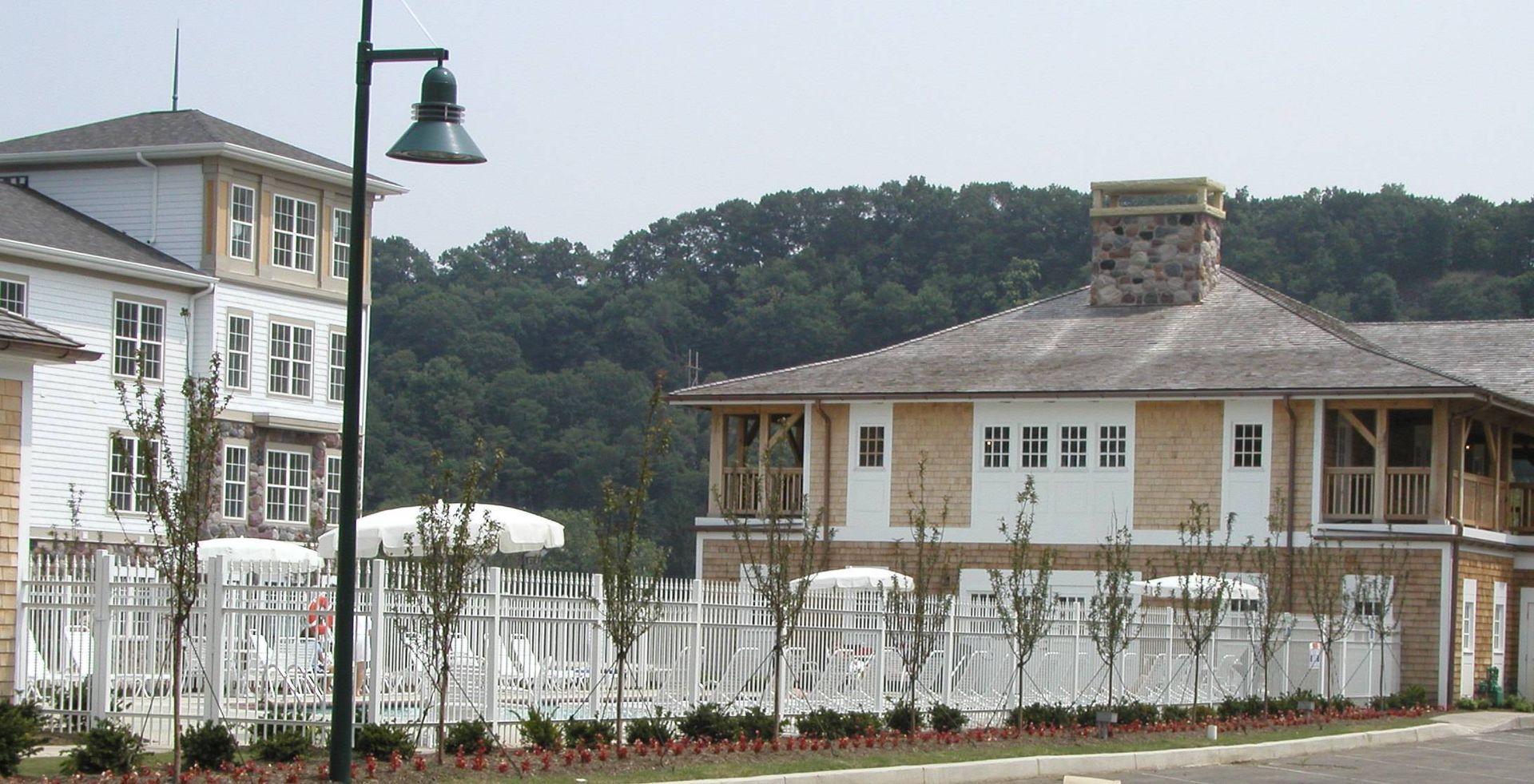 White cottage-style house with a stone chimney behind a white fence, near a streetlamp and trees