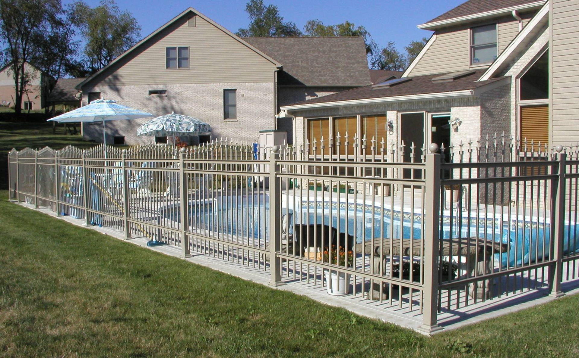 Backyard swimming pool enclosed by a white fence beside a house on a sunny day
