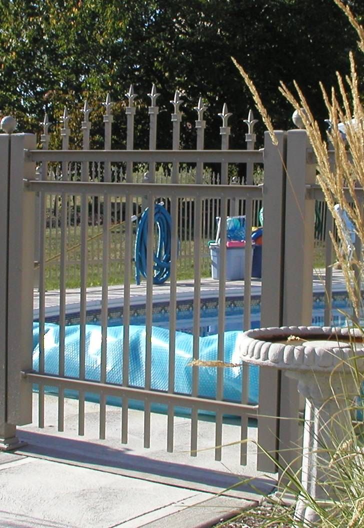 Metal gate beside a blue swimming pool and stone planter in a sunny yard
