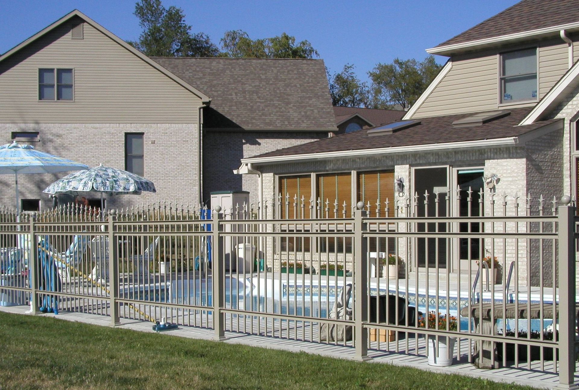 Outdoor apartment pool area with blue lounge chairs, umbrellas, and a metal fence beside buildings