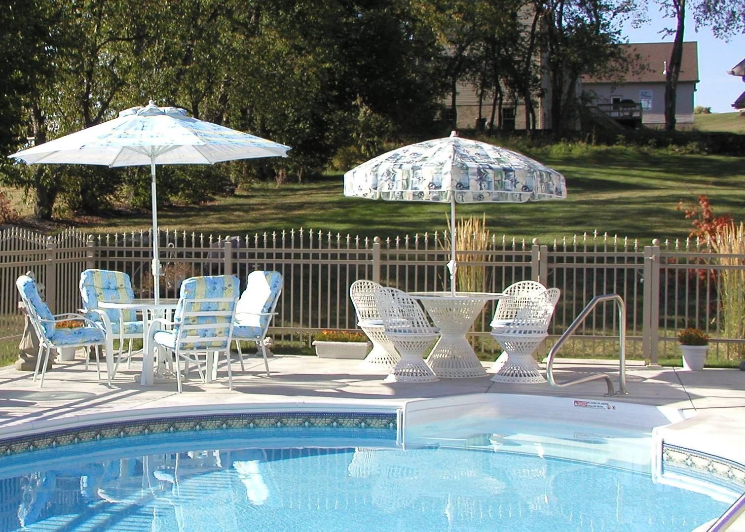 Poolside patio with white chairs, umbrellas, and a swimming pool in the foreground