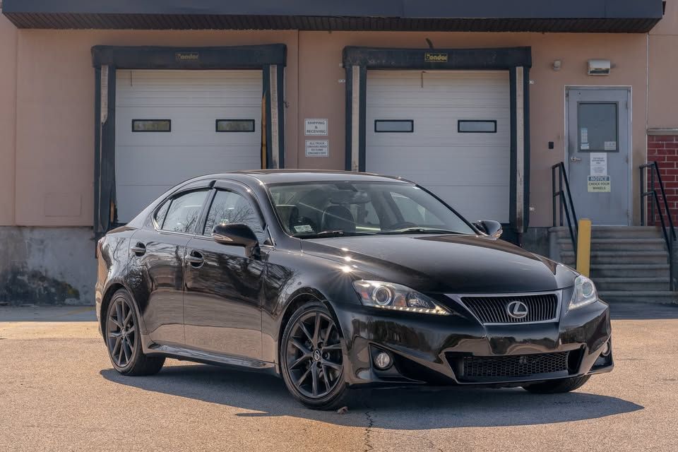 A black lexus is parked in front of a warehouse.