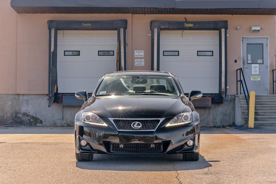 A black lexus is parked in front of a warehouse.