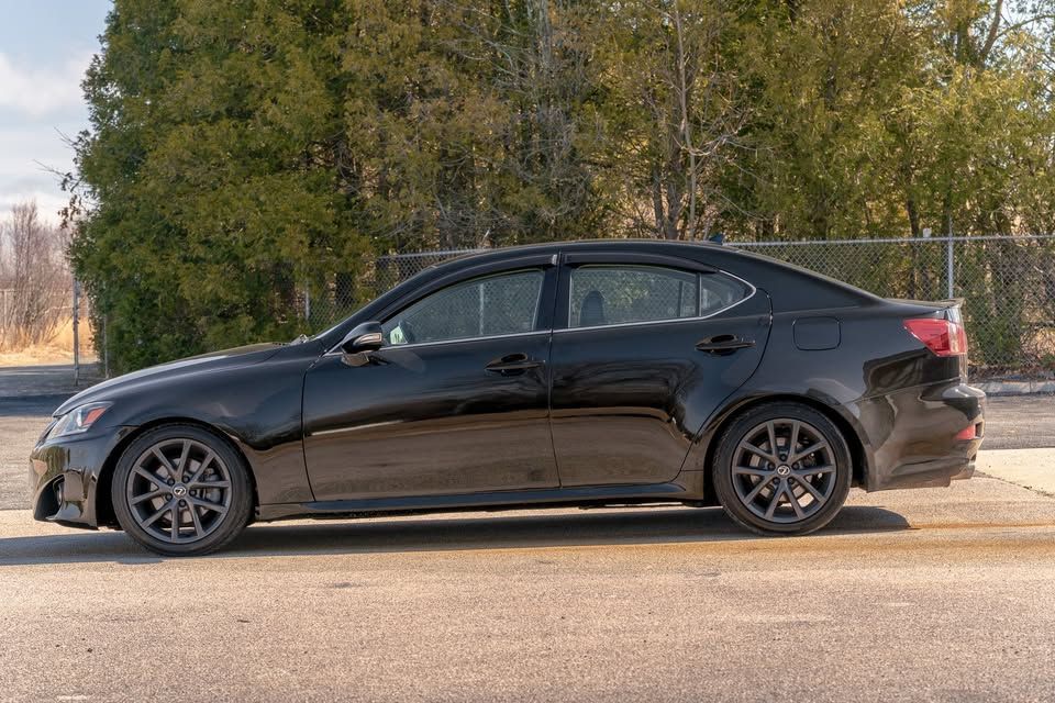 A black car is parked in a parking lot next to a fence.