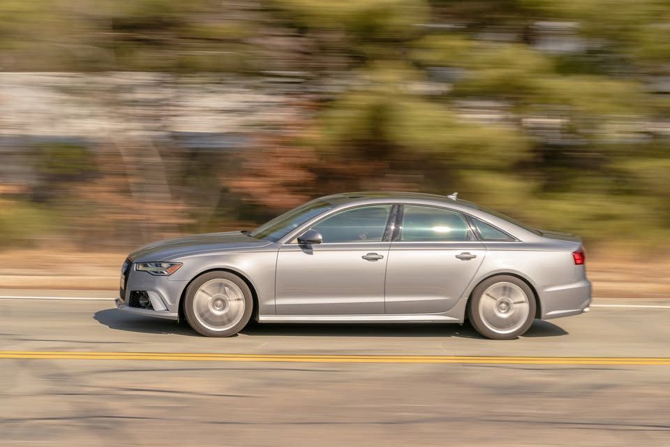 A silver audi a6 is driving down a road.