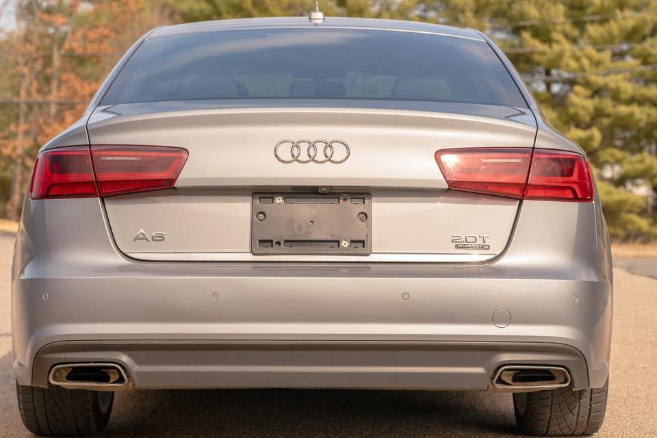 The rear end of a silver audi a6 is parked on the side of the road.