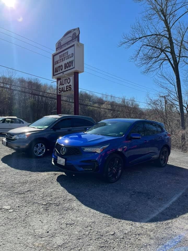 Two blue cars are parked in front of the North Smithfield Auto Body Inc signage