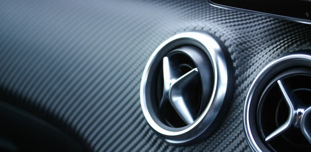 Close-up of Mercedes-Benz and AMG emblems on a carbon-fiber car grille