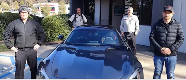 Three people standing beside a dark blue sports car in a parking lot