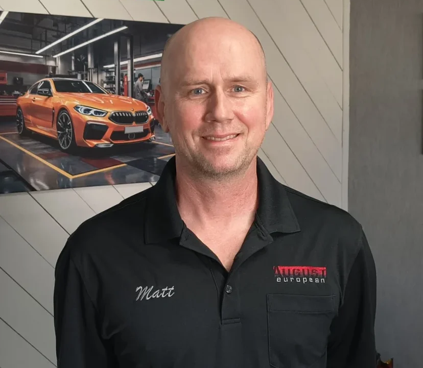 Man in black shirt standing indoors beside an orange sports car photo