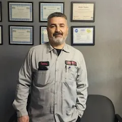 Man in gray work shirt standing indoors in front of framed certificates on a wall