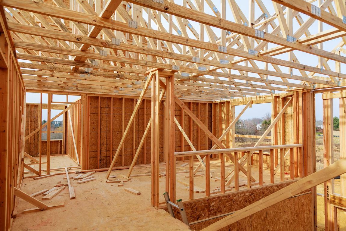 Wood framing structure of a residential house under construction, showing exposed studs, beams, and roof trusses in a partially built home on a clear day.