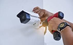 Hand installing a white security camera on a wall with a power drill