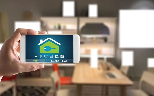 Hand holding a smartphone showing a smart home app in a blurred modern kitchen