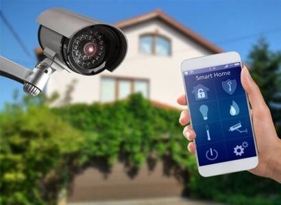 Home security camera beside a smartphone showing smart home controls in front of a house