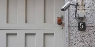 White exterior wall with a red alarm light and a black house number 5 plaque near a doorway